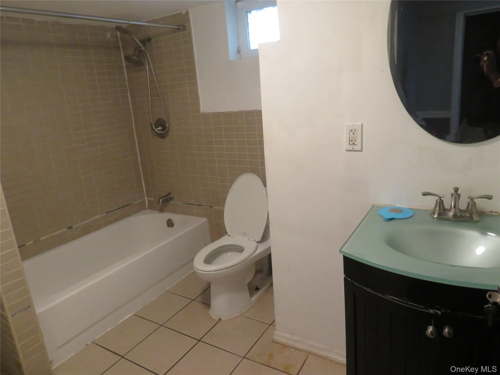 Bathroom featuring a white bathtub, tiled shower surround, commode, and a vanity with a frosted glass basin Bathroom featuring a white bathtub, tiled shower surround, commode, and a vanity with a frosted glass basin