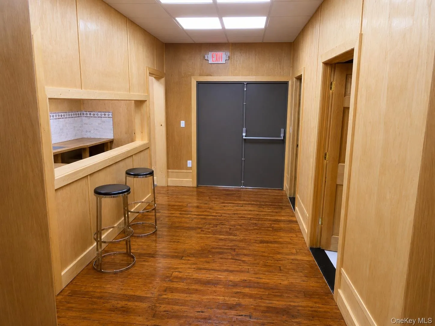 Hallway featuring wood-finish flooring, light wood paneling, and a built-in service counter with decorative tile backsplash Hallway featuring wood-finish flooring, light wood paneling, and a built-in service counter with decorative tile backsplash