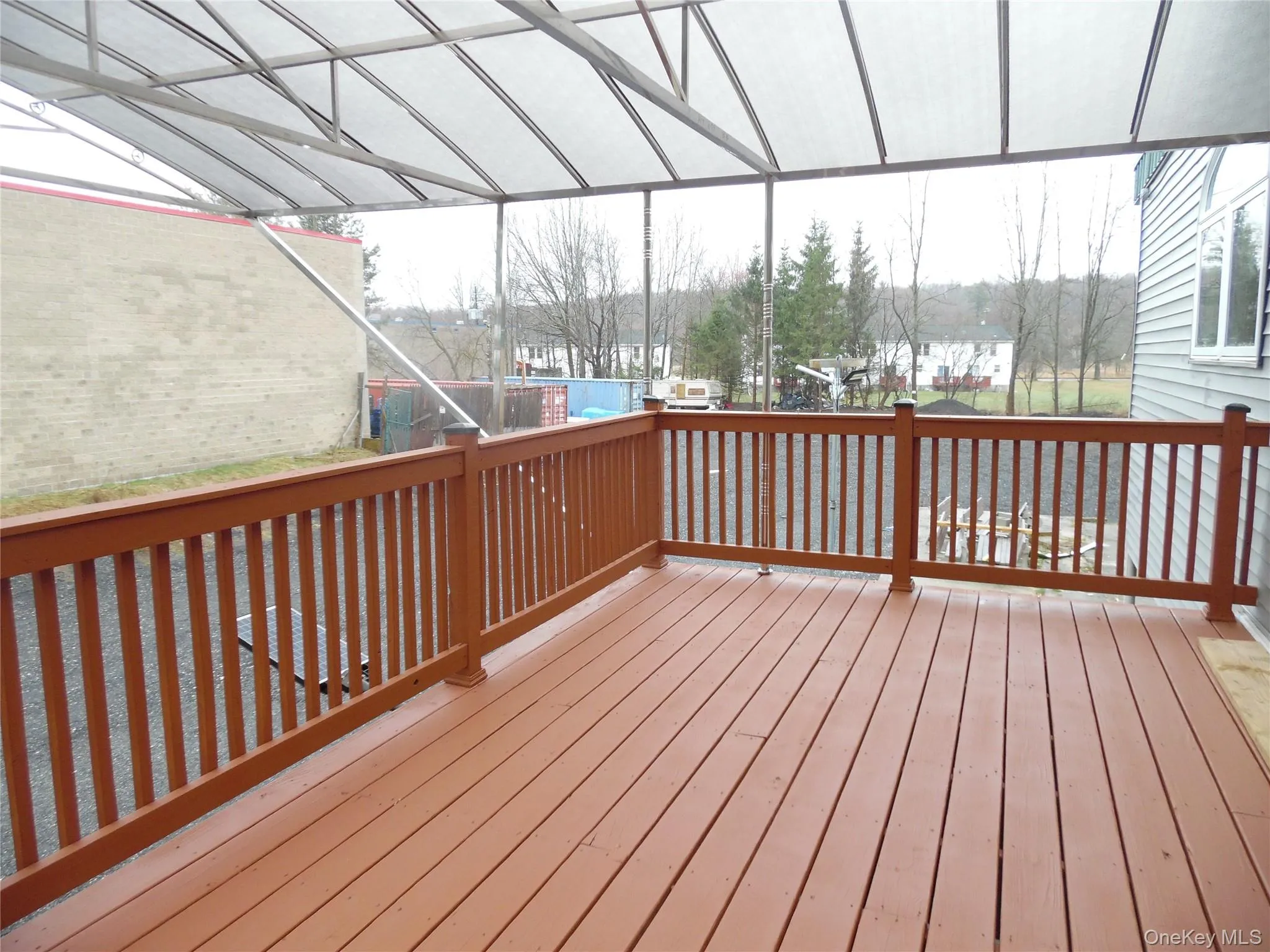 Expansive outdoor deck featuring a brown wood-finish surface, matching railing, and an overhead translucent awning Expansive outdoor deck featuring a brown wood-finish surface, matching railing, and an overhead translucent awning