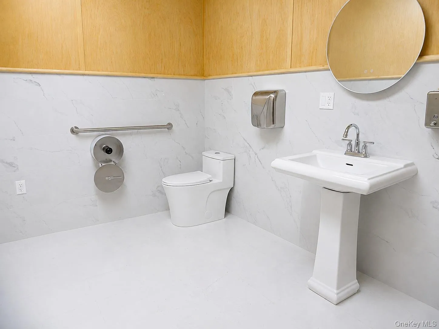 Pedestal sink with chrome faucet, white toilet, and white marble-look wall tiling Pedestal sink with chrome faucet, white toilet, and white marble-look wall tiling