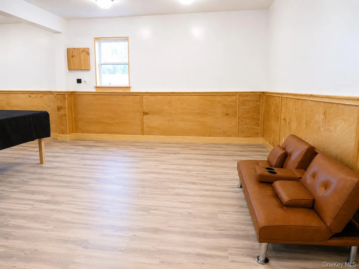 Spacious room featuring light wood-finish flooring, white walls, and a lower half adorned with wood paneling and trim Spacious room featuring light wood-finish flooring, white walls, and a lower half adorned with wood paneling and trim