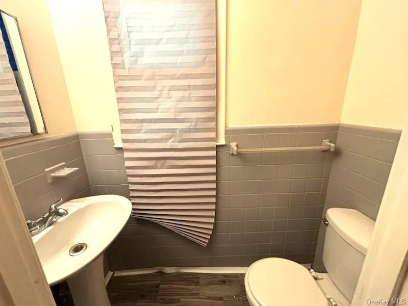 Bathroom with tile walls, a wainscoted wall, and dark wood-style floors Bathroom with tile walls, a wainscoted wall, and dark wood-style floors