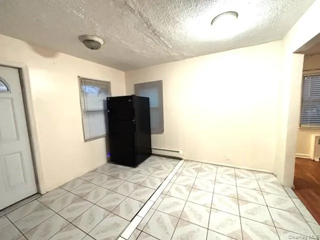 Kitchen with freestanding refrigerator, a textured ceiling, a baseboard radiator, and light tile patterned floors Kitchen with freestanding refrigerator, a textured ceiling, a baseboard radiator, and light tile patterned floors