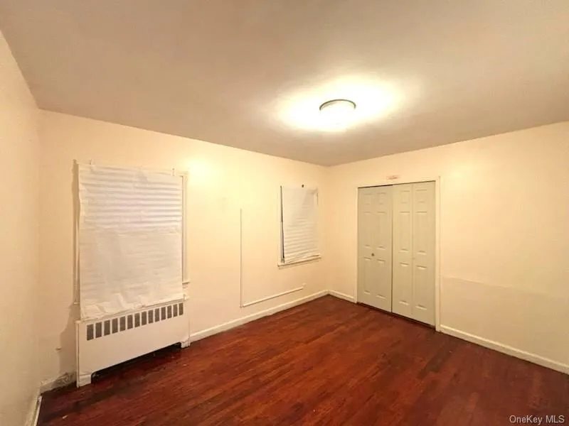 Unfurnished bedroom with radiator, dark wood finished floors, and a closet Unfurnished bedroom with radiator, dark wood finished floors, and a closet