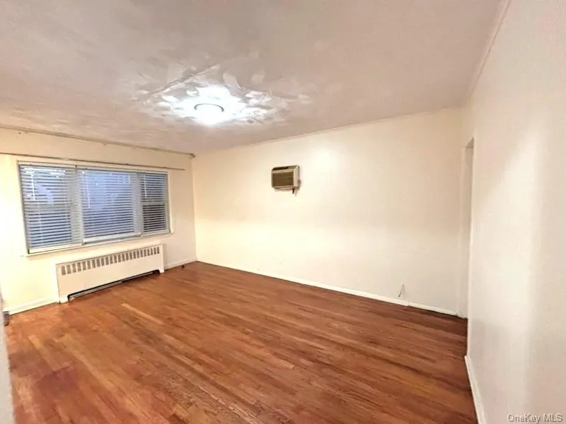 Unfurnished room with radiator heating unit, wood finished floors, and a wall mounted AC Unfurnished room with radiator heating unit, wood finished floors, and a wall mounted AC