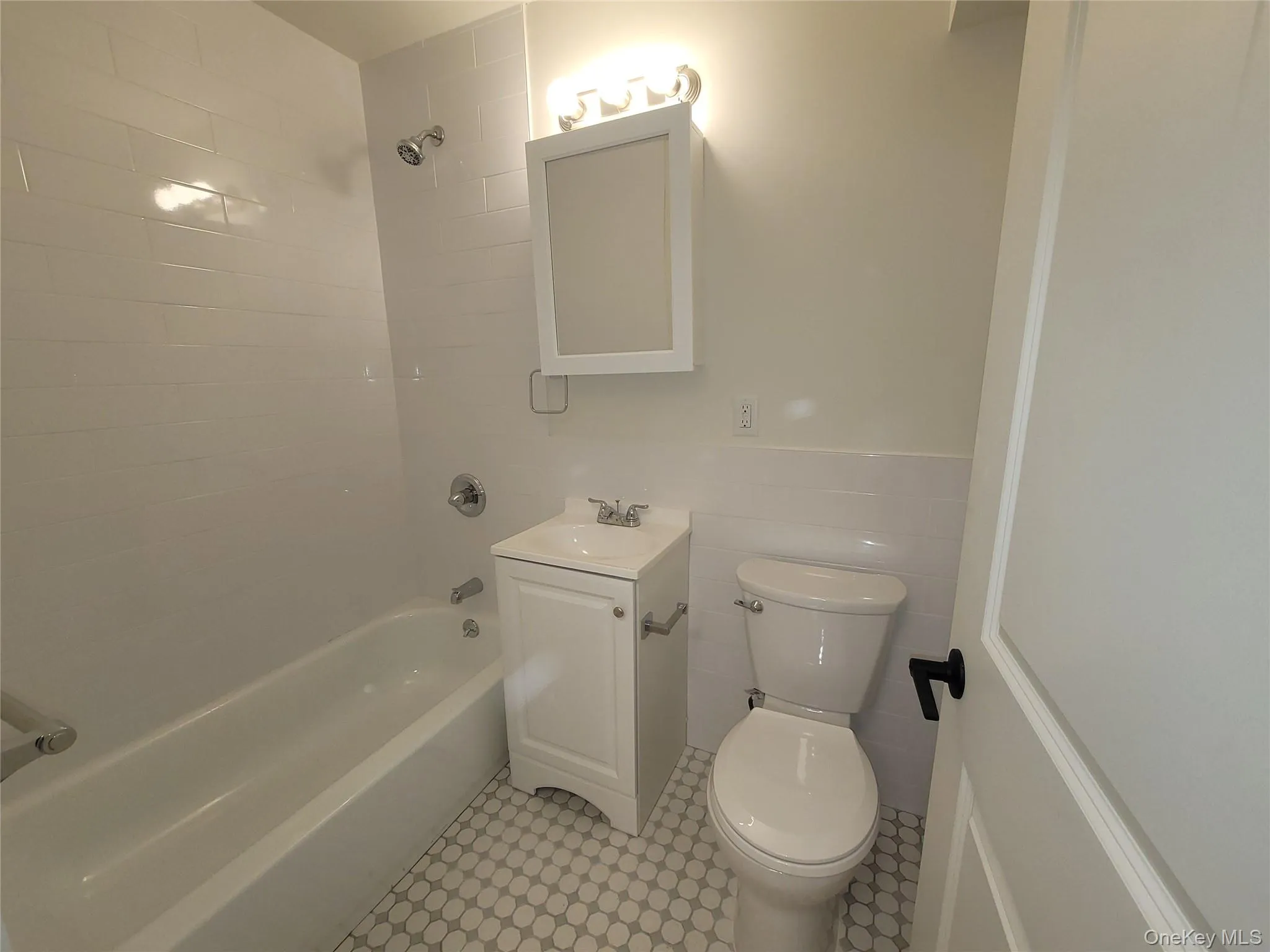 Bathroom featuring a white subway tile surround, white vanity with integrated sink, chrome fixtures, a medicine cabinet, and penny tile flooring Bathroom featuring a white subway tile surround, white vanity with integrated sink, chrome fixtures, a medicine cabinet, and penny tile flooring
