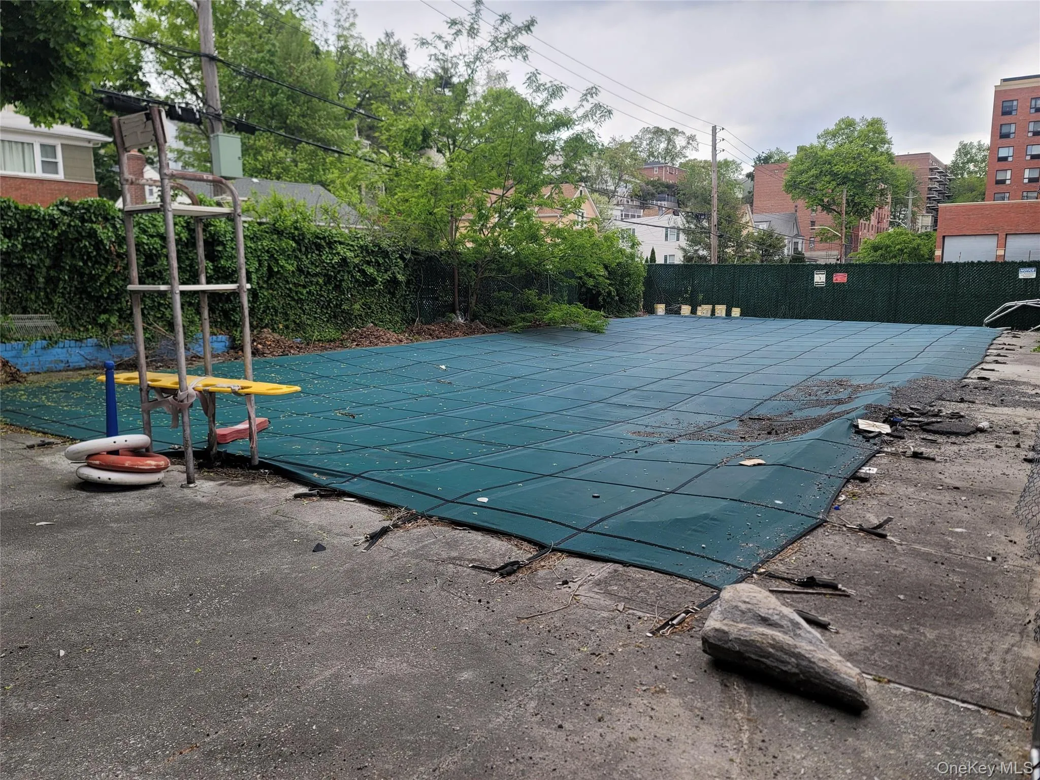 Outdoor pool area featuring a green safety cover, perimeter fencing, and a concrete patio Outdoor pool area featuring a green safety cover, perimeter fencing, and a concrete patio