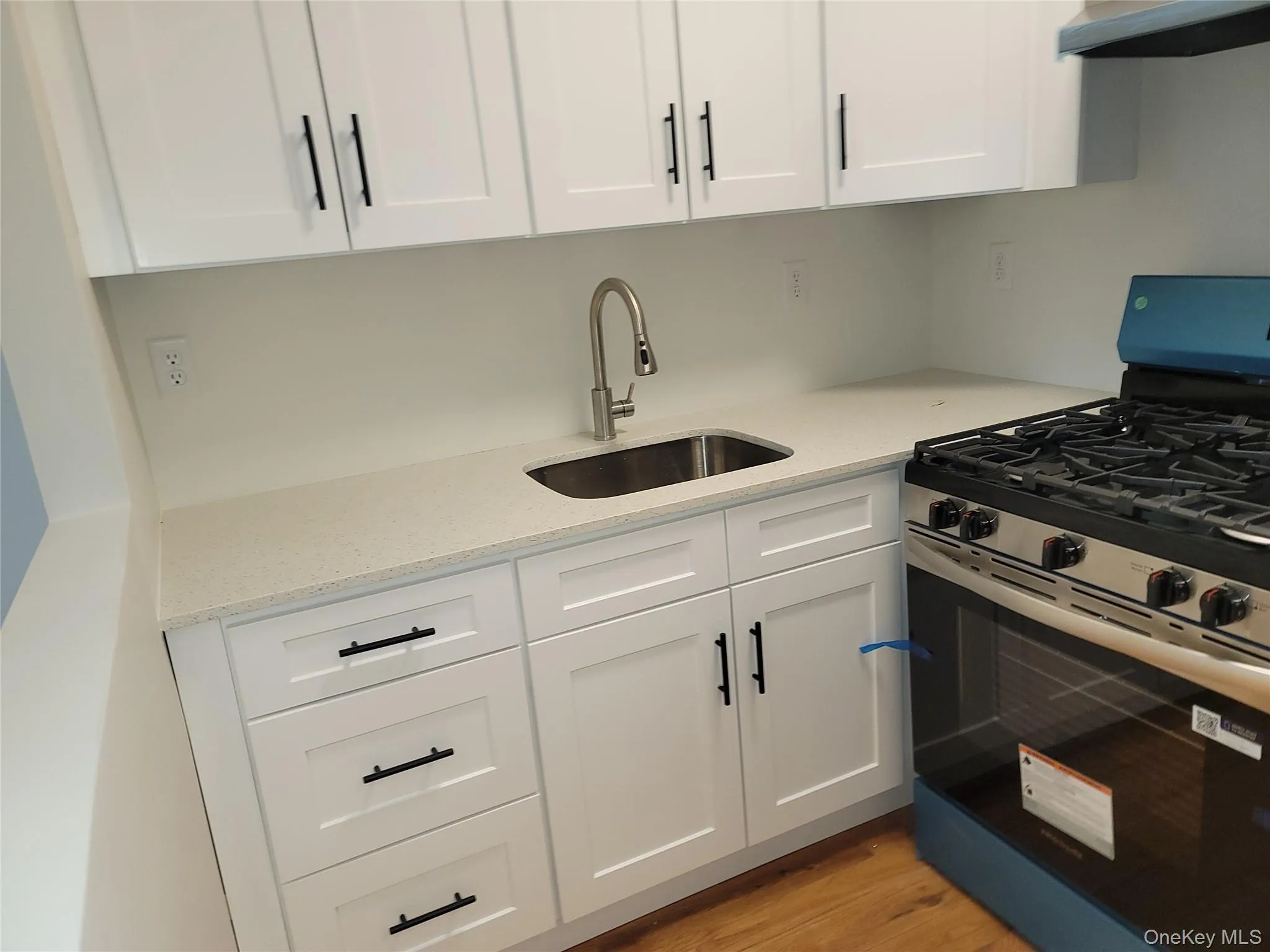 Contemporary kitchen featuring white shaker cabinetry, black hardware, stainless steel sink, and a new gas range Contemporary kitchen featuring white shaker cabinetry, black hardware, stainless steel sink, and a new gas range