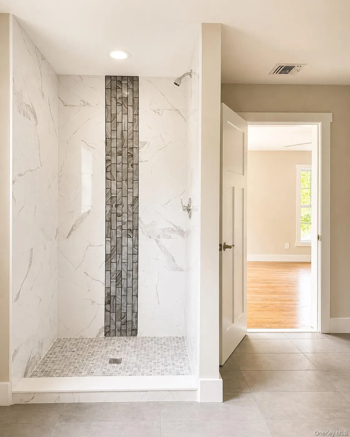 Walk-in shower with white marbled tile walls, a vertical accent strip of rectangular mosaic tiles, and a mosaic tile floor Walk-in shower with white marbled tile walls, a vertical accent strip of rectangular mosaic tiles, and a mosaic tile floor