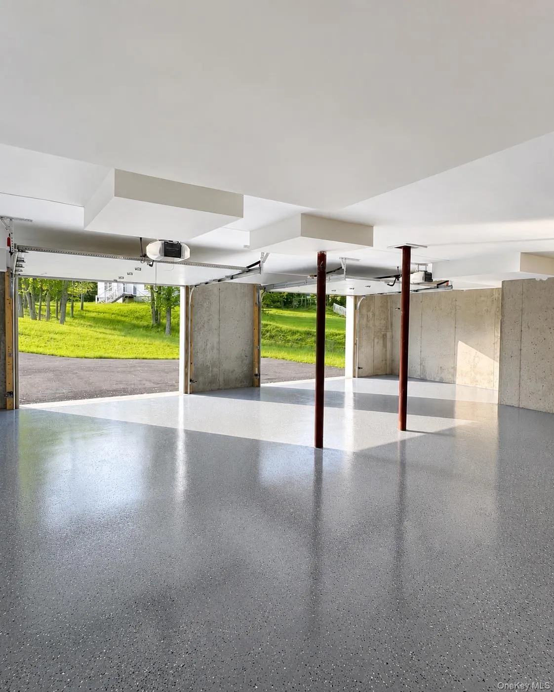 Spacious garage featuring a speckled epoxy floor finish and concrete walls Spacious garage featuring a speckled epoxy floor finish and concrete walls