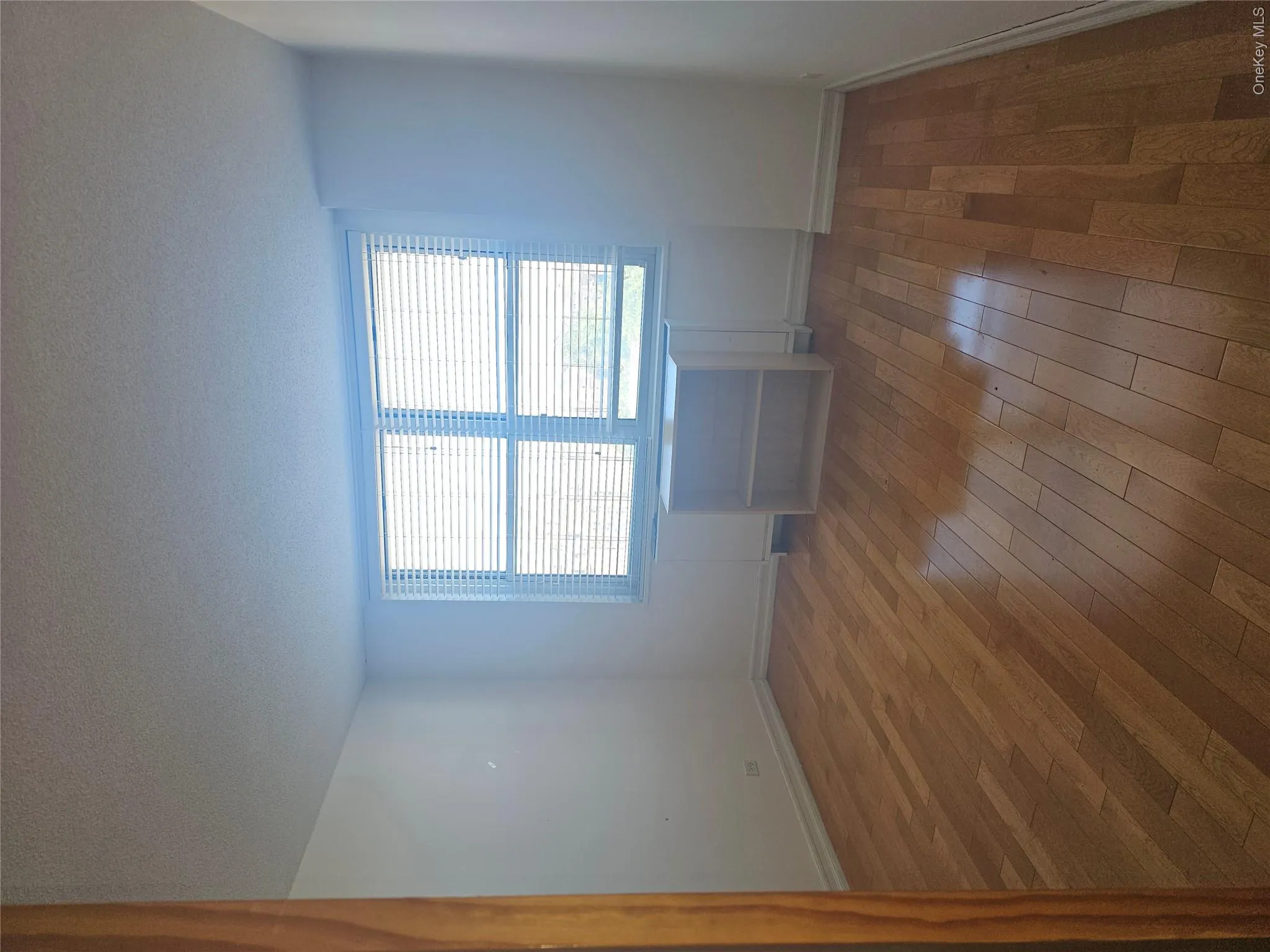 Spacious interior room with wood-finish flooring, white walls, and a large window with horizontal blinds Spacious interior room with wood-finish flooring, white walls, and a large window with horizontal blinds