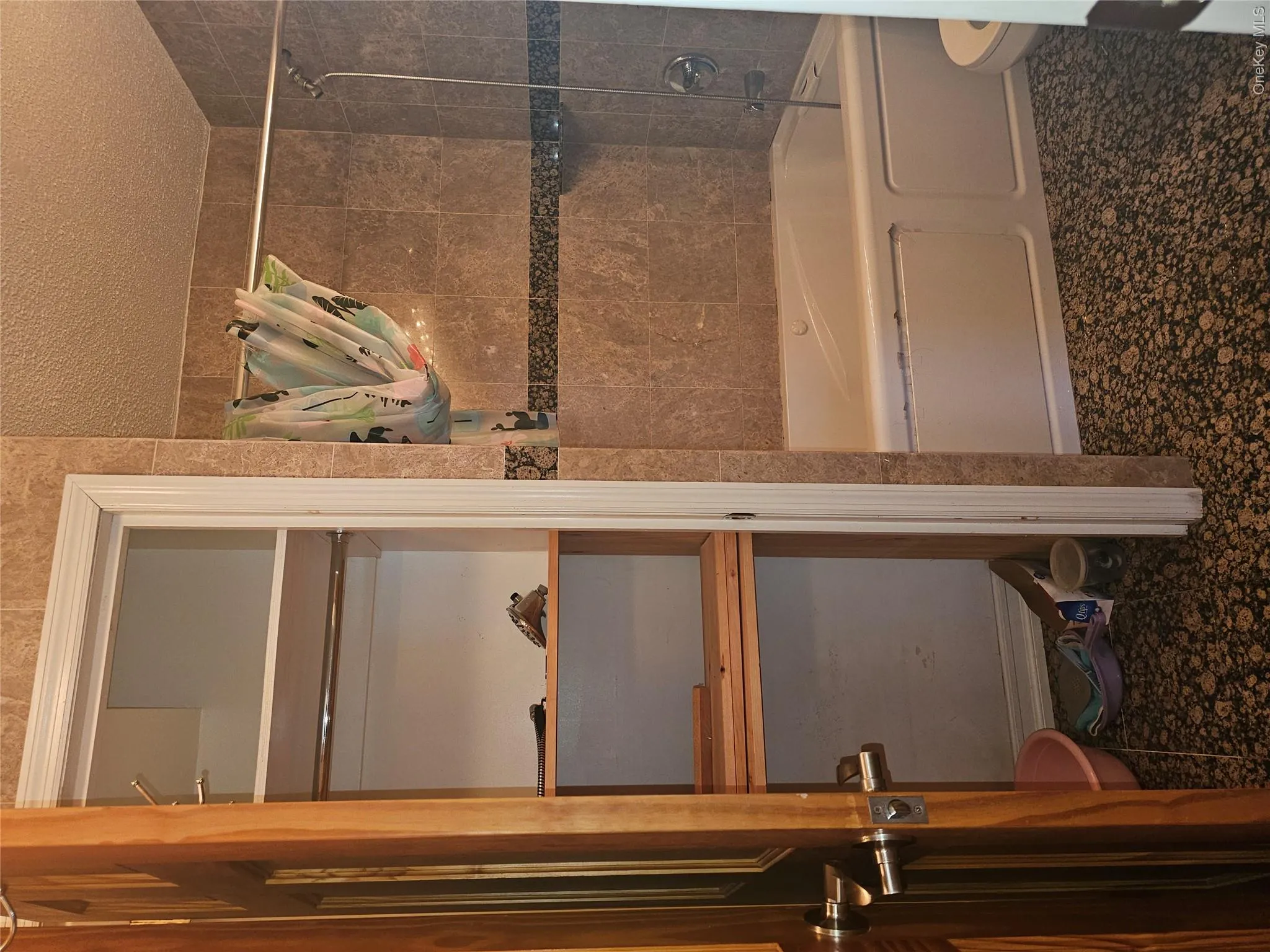 Bathroom featuring a built-in tub with tile surround, a dark patterned floor, and a full-height closet with shelving and a hanging rod Bathroom featuring a built-in tub with tile surround, a dark patterned floor, and a full-height closet with shelving and a hanging rod