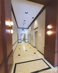 Hallway featuring sconce lighting, recessed ceiling lights, wood-paneled walls, and patterned tile flooring Hallway featuring sconce lighting, recessed ceiling lights, wood-paneled walls, and patterned tile flooring