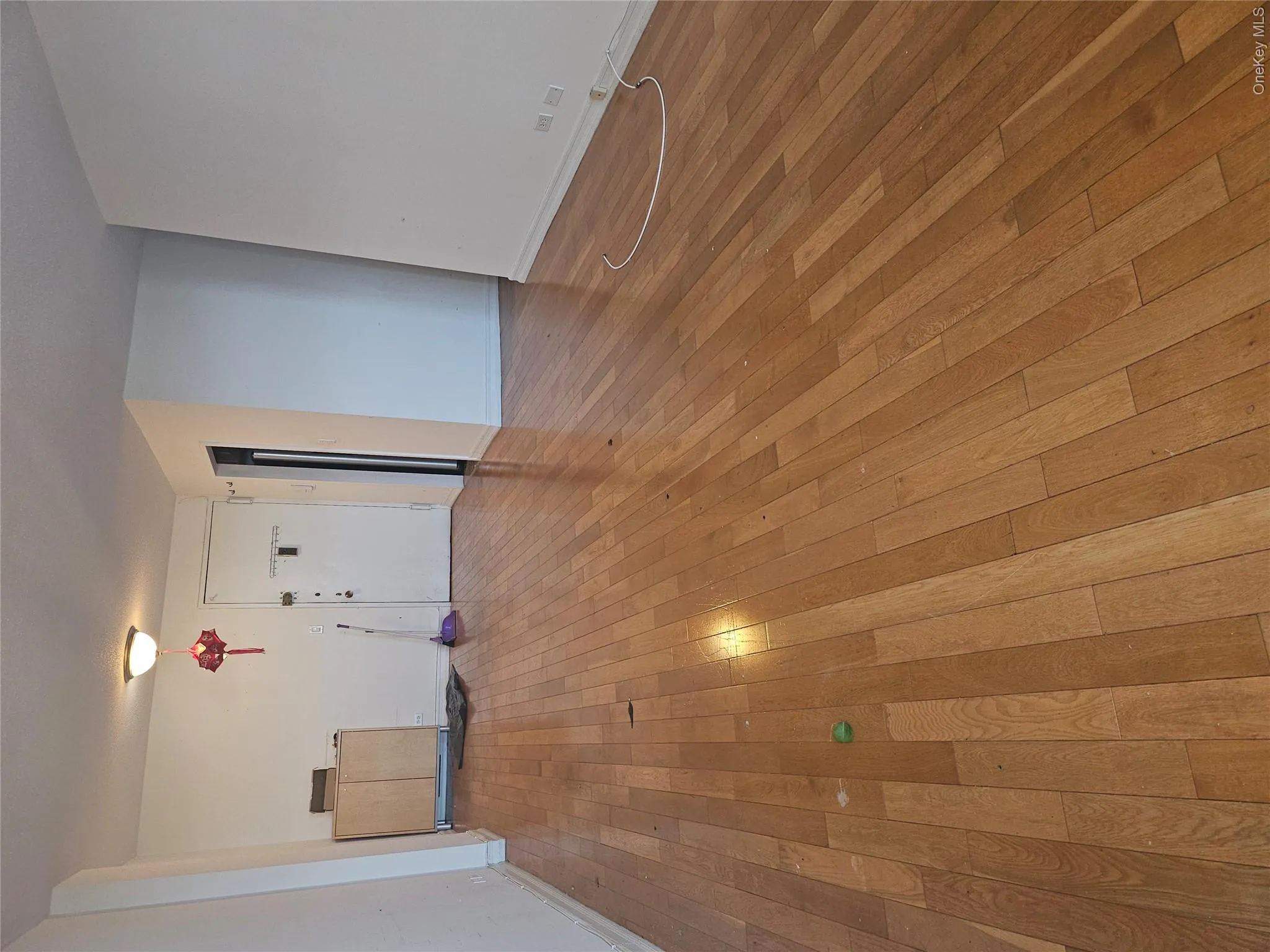 Spacious room featuring wood-finish flooring, white walls, and a ceiling-mounted light fixture Spacious room featuring wood-finish flooring, white walls, and a ceiling-mounted light fixture