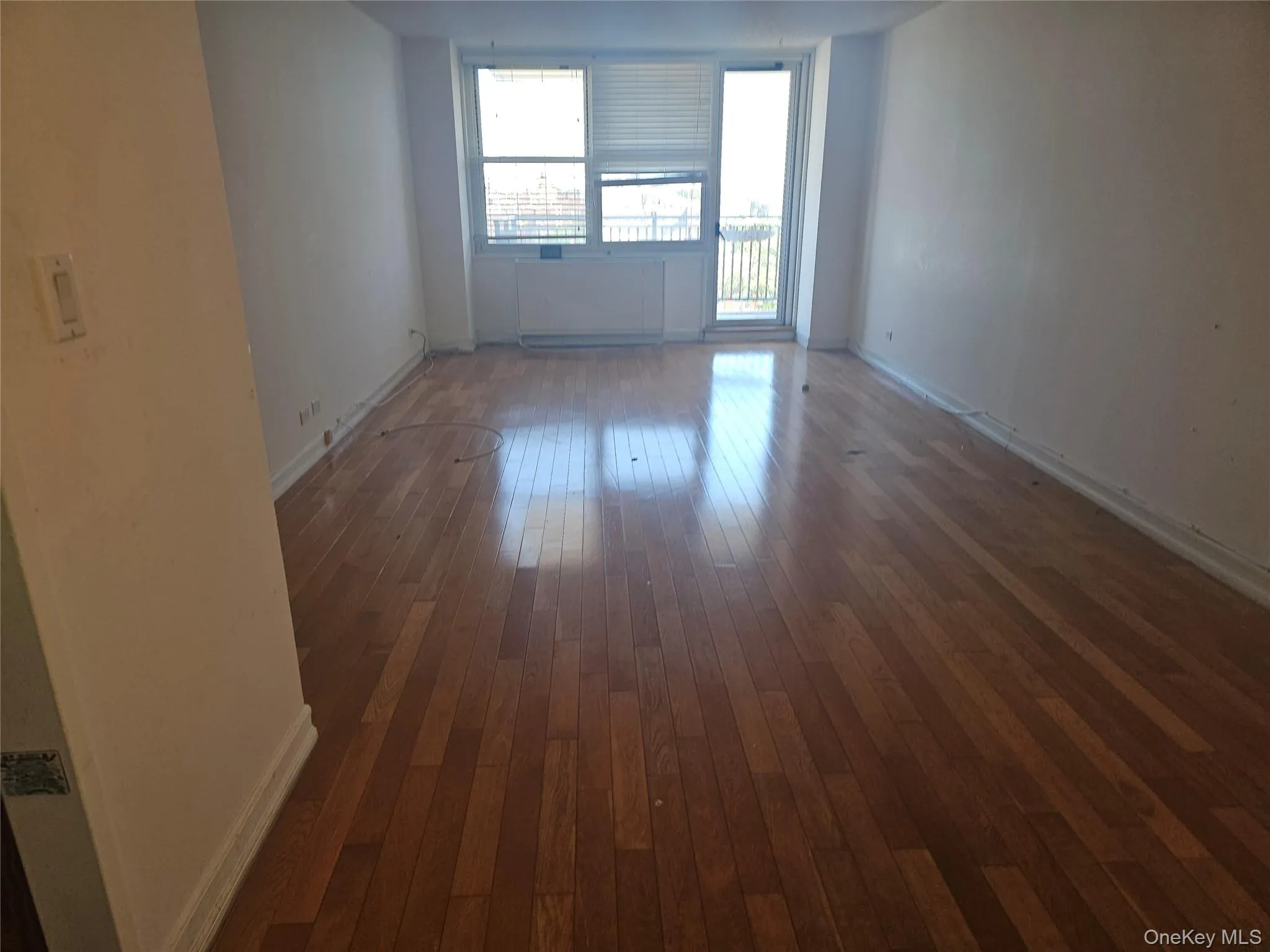 Spacious room featuring wood-finish flooring, white walls, and a ceiling-mounted light fixture Spacious room featuring wood-finish flooring, white walls, and a ceiling-mounted light fixture
