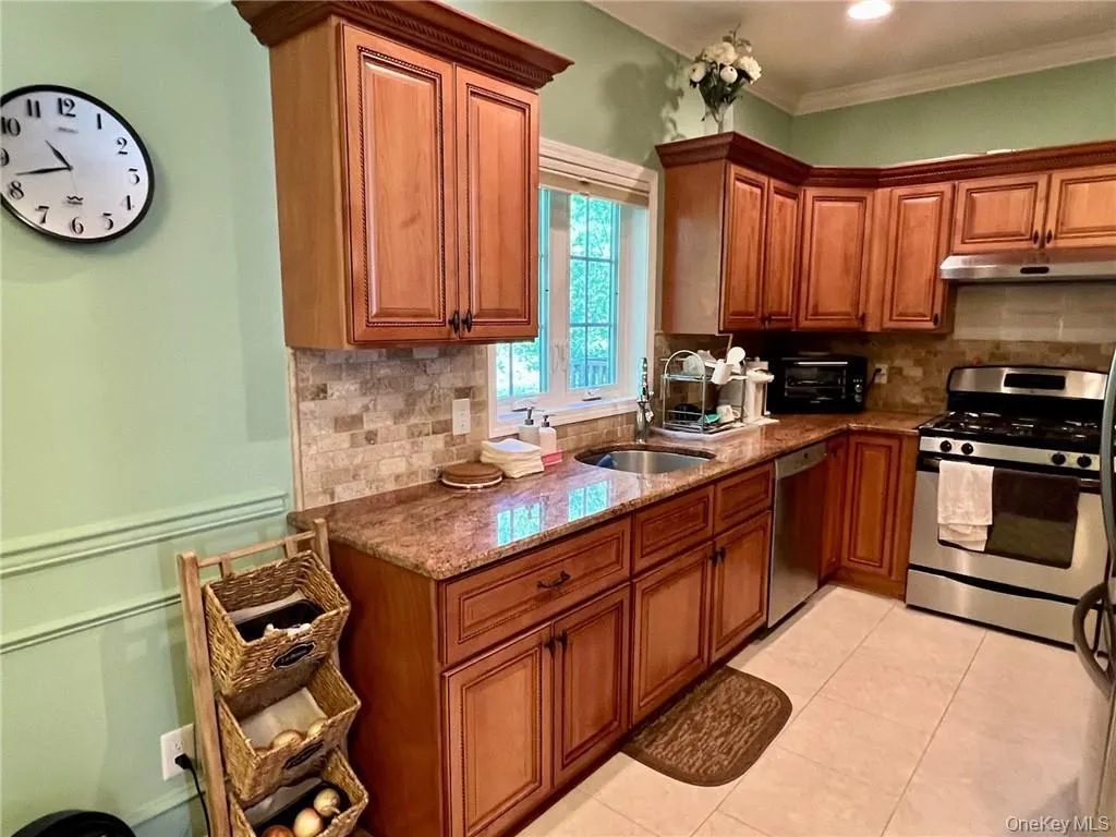 Kitchen with appliances with stainless steel finishes, brown cabinetry, under cabinet range hood, backsplash, and crown molding Kitchen with appliances with stainless steel finishes, brown cabinetry, under cabinet range hood, backsplash, and crown molding