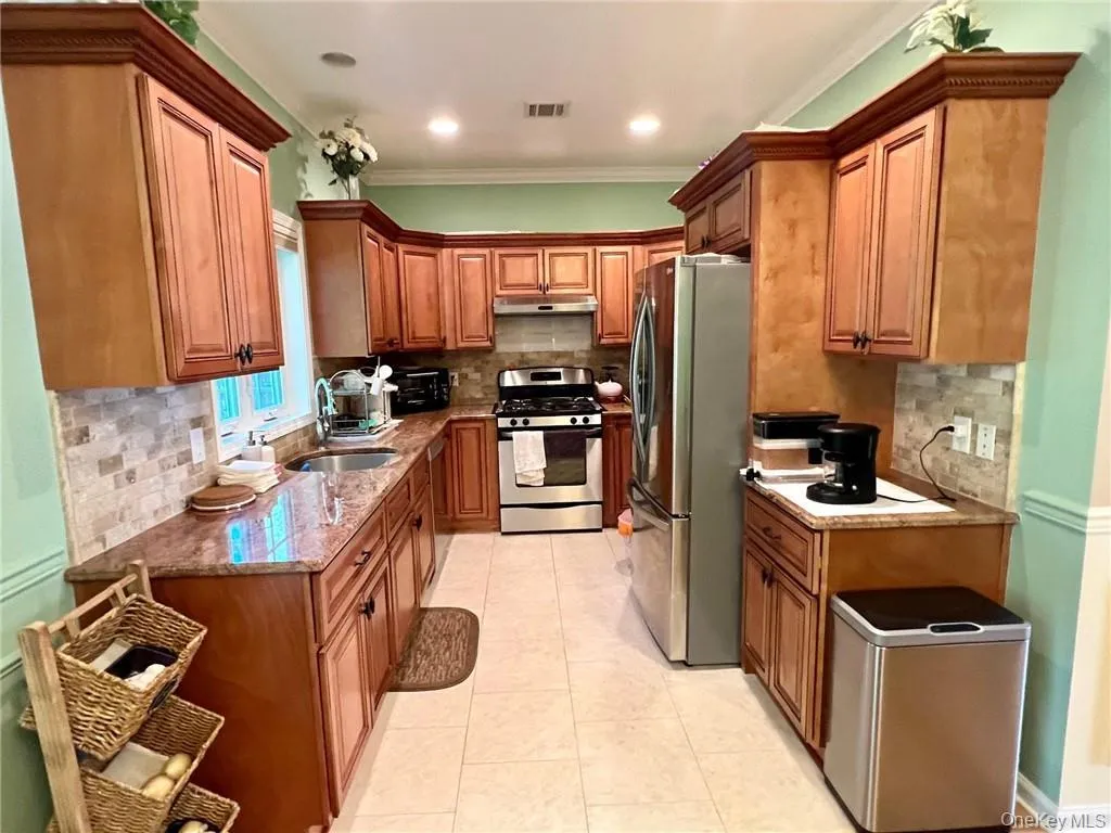 Kitchen featuring stainless steel appliances, a sink, under cabinet range hood, decorative backsplash, and crown molding Kitchen featuring stainless steel appliances, a sink, under cabinet range hood, decorative backsplash, and crown molding