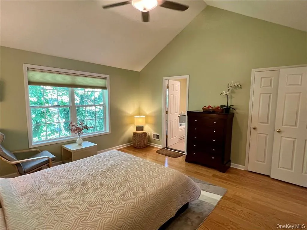 Bedroom featuring wood finished floors, baseboards, high vaulted ceiling, ensuite bath, and ceiling fan Bedroom featuring wood finished floors, baseboards, high vaulted ceiling, ensuite bath, and ceiling fan