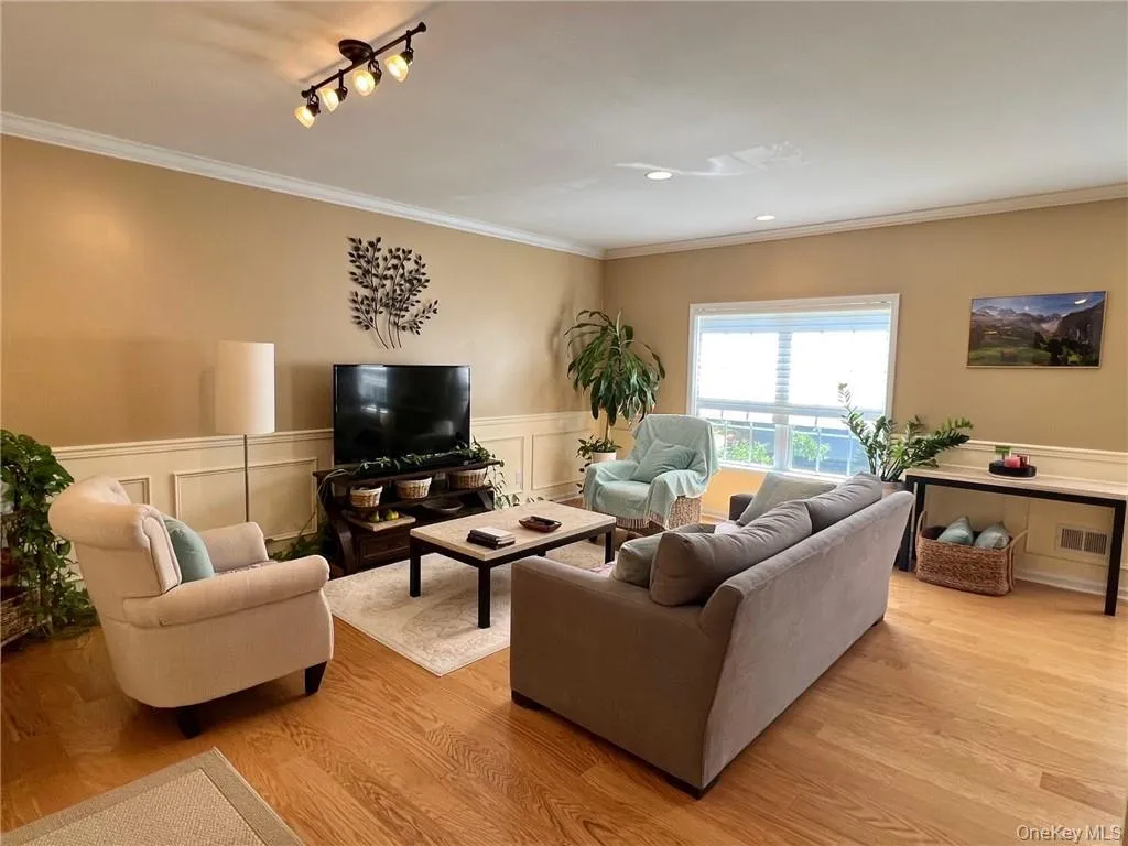 Living room featuring crown molding, wainscoting, light wood-style flooring, a decorative wall, and track lighting Living room featuring crown molding, wainscoting, light wood-style flooring, a decorative wall, and track lighting
