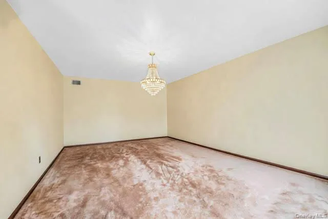 Spacious room featuring a tiered crystal chandelier, light-toned wall paint, and a brown baseboard trim Spacious room featuring a tiered crystal chandelier, light-toned wall paint, and a brown baseboard trim