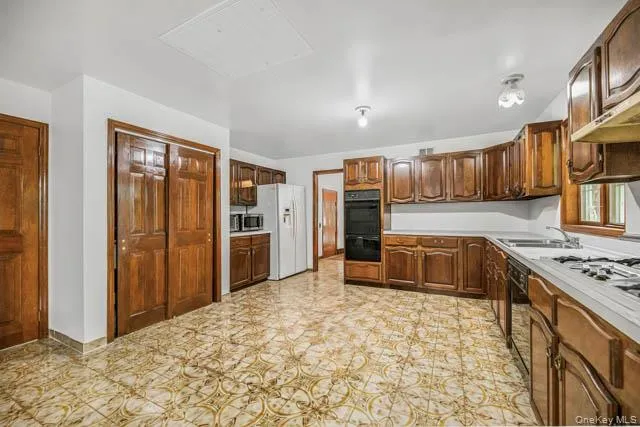 Kitchen featuring wood-finish cabinetry, patterned floor tiles, built-in oven, wall-mounted microwave, and recessed lighting Kitchen featuring wood-finish cabinetry, patterned floor tiles, built-in oven, wall-mounted microwave, and recessed lighting