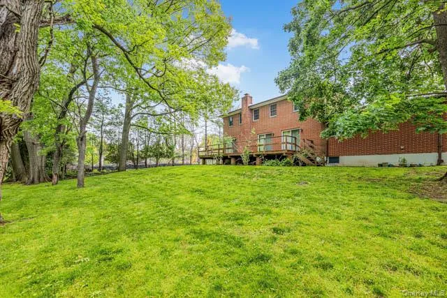 Expansive rear lawn featuring mature trees and a brick exterior with a wooden deck Expansive rear lawn featuring mature trees and a brick exterior with a wooden deck