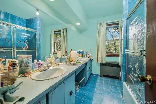 Bathroom featuring dual vanity with integrated sinks, expansive mirror, track lighting, and a window with natural light Bathroom featuring dual vanity with integrated sinks, expansive mirror, track lighting, and a window with natural light