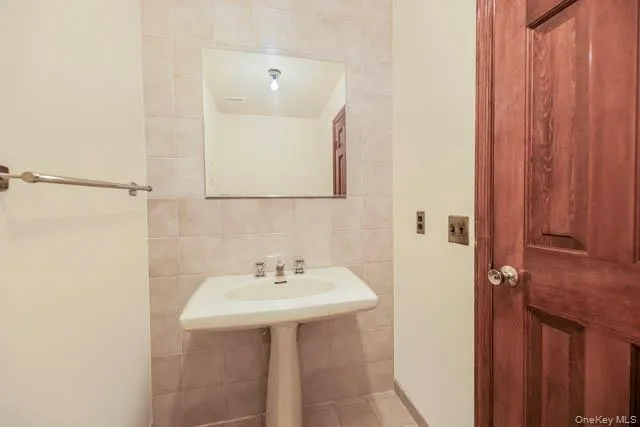 Pedestal sink with dual-handle faucet, set against tiled walls and a frameless wall-mounted mirror Pedestal sink with dual-handle faucet, set against tiled walls and a frameless wall-mounted mirror