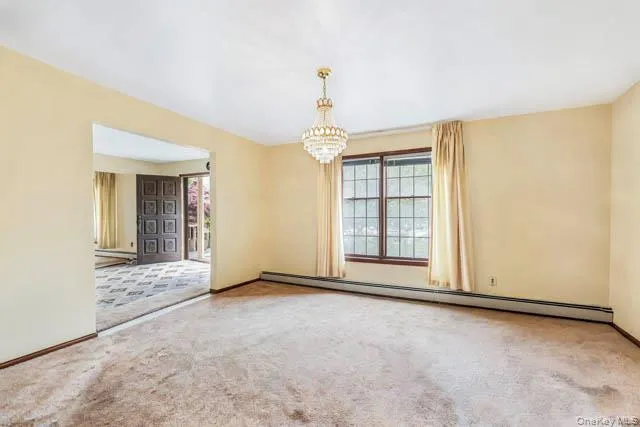 Spacious room featuring a crystal chandelier, large window with drapes, and neutral-toned walls Spacious room featuring a crystal chandelier, large window with drapes, and neutral-toned walls