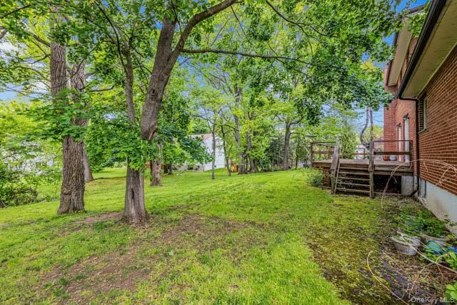 Expansive green space featuring a multi-level wood deck, mature trees, and a brick exterior Expansive green space featuring a multi-level wood deck, mature trees, and a brick exterior