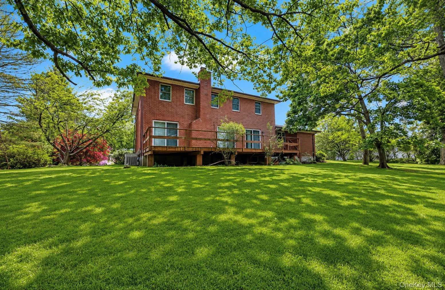 Spacious backyard with mature trees, a red brick exterior, multiple windows, a wooden deck, and sliding glass doors Spacious backyard with mature trees, a red brick exterior, multiple windows, a wooden deck, and sliding glass doors