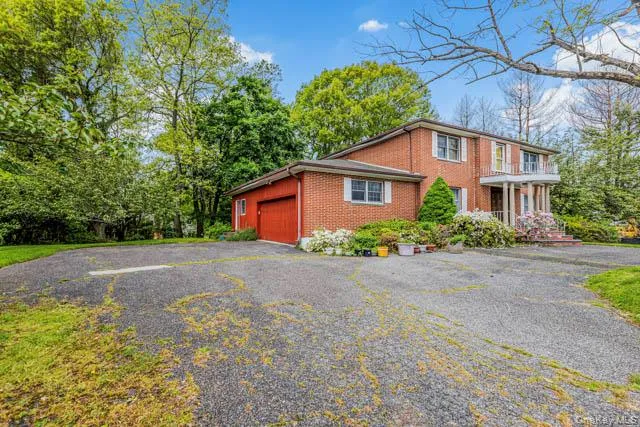 Brick exterior residence featuring a red garage door, white-trimmed windows, and a columned entry with an upper-level balcony Brick exterior residence featuring a red garage door, white-trimmed windows, and a columned entry with an upper-level balcony