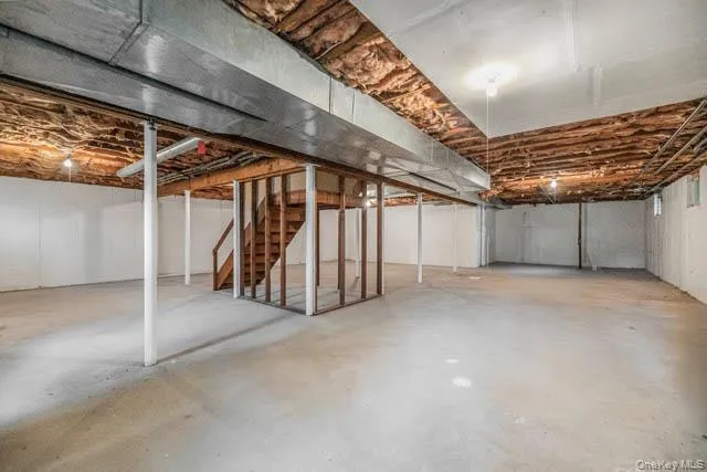 Expansive unfinished basement featuring concrete flooring, exposed wood joists, white painted walls, and a visible wood staircase Expansive unfinished basement featuring concrete flooring, exposed wood joists, white painted walls, and a visible wood staircase