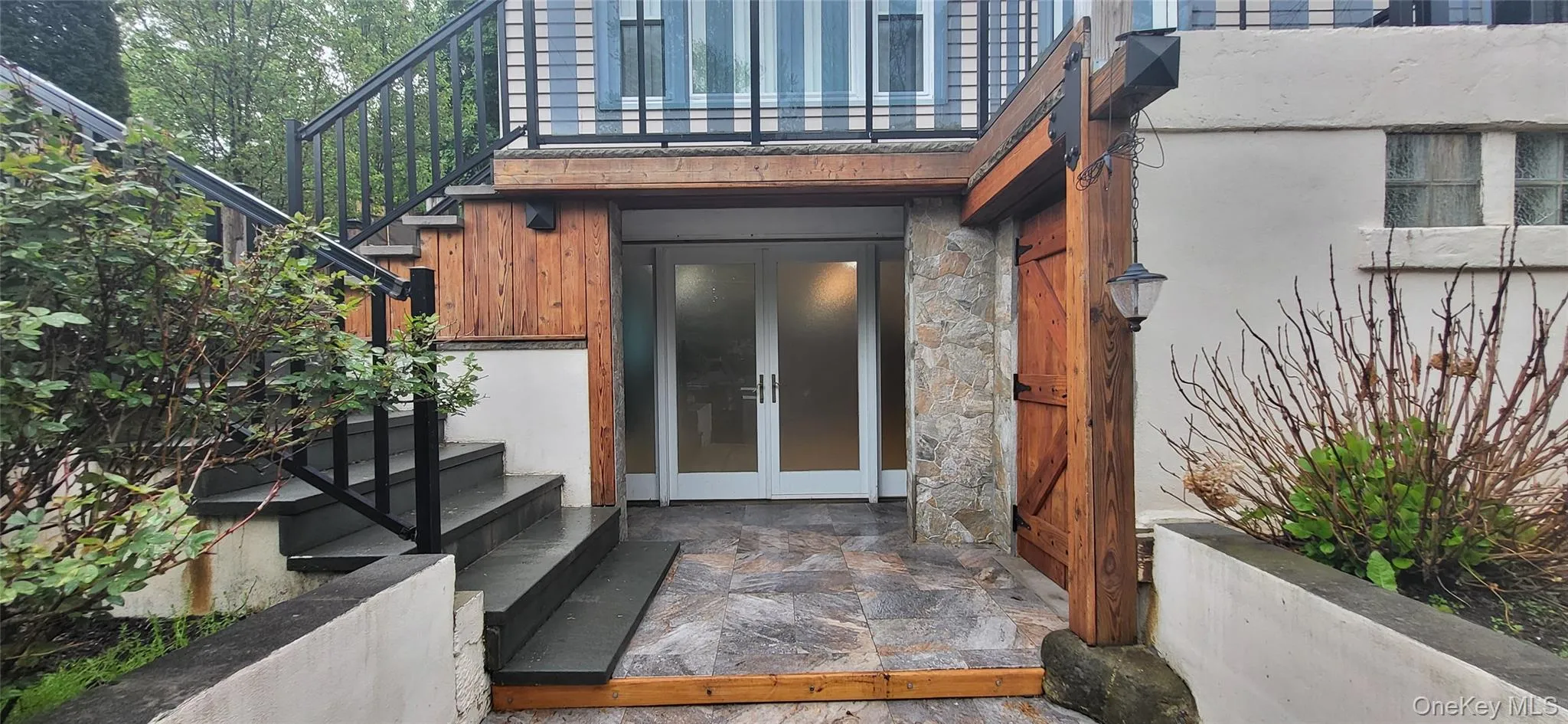Stone tile patio leading to frosted glass double entry doors, complemented by a stone facade and wood accents Stone tile patio leading to frosted glass double entry doors, complemented by a stone facade and wood accents