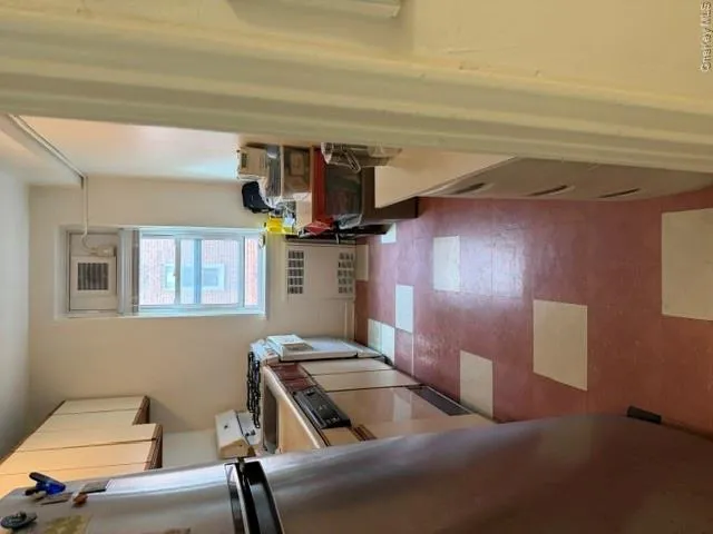 Galley kitchen featuring a window with an integrated air conditioning unit, white upper cabinetry, and a stainless steel refrigerator Galley kitchen featuring a window with an integrated air conditioning unit, white upper cabinetry, and a stainless steel refrigerator