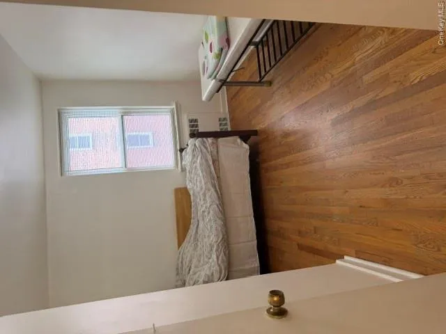 Spacious room featuring wood-finish flooring, white walls, and a double-hung window with blinds Spacious room featuring wood-finish flooring, white walls, and a double-hung window with blinds