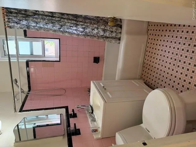 Bathroom featuring pink and black tiled walls, a white bathtub with a shower kit, a white vanity with an integrated sink, a white toilet, and patterned floor tiling Bathroom featuring pink and black tiled walls, a white bathtub with a shower kit, a white vanity with an integrated sink, a white toilet, and patterned floor tiling