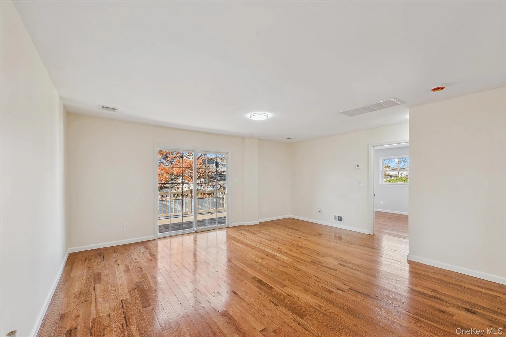 Spacious living area featuring wood-finish flooring, light neutral walls, and a large sliding glass door with a balcony Spacious living area featuring wood-finish flooring, light neutral walls, and a large sliding glass door with a balcony