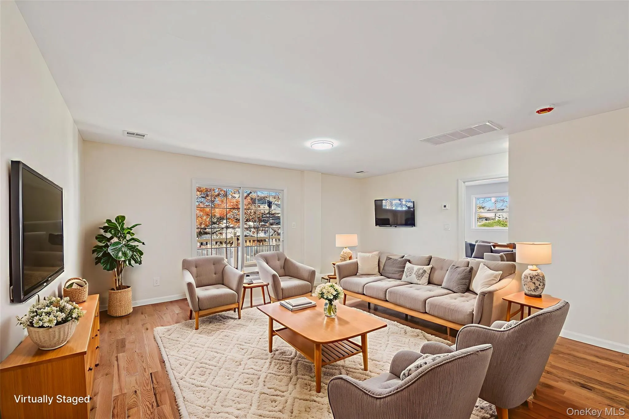 Spacious living area featuring wood-finish flooring, light neutral walls, and a large sliding glass door with a balcony Spacious living area featuring wood-finish flooring, light neutral walls, and a large sliding glass door with a balcony