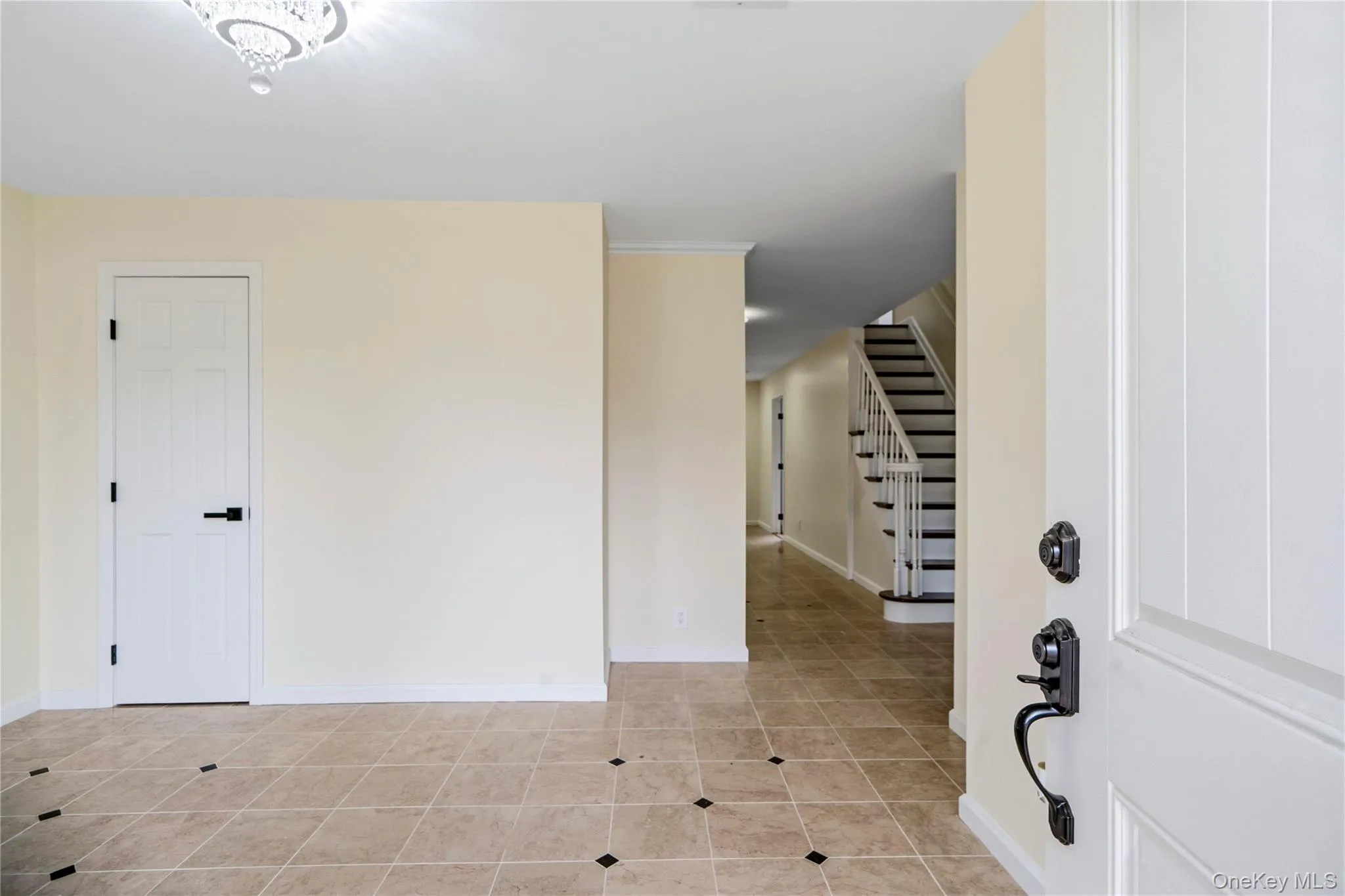 Inviting entryway featuring light-toned tile flooring with dark accent tiles, a white paneled door with matte black hardware, and a grand staircase with white risers and dark treads Inviting entryway featuring light-toned tile flooring with dark accent tiles, a white paneled door with matte black hardware, and a grand staircase with white risers and dark treads