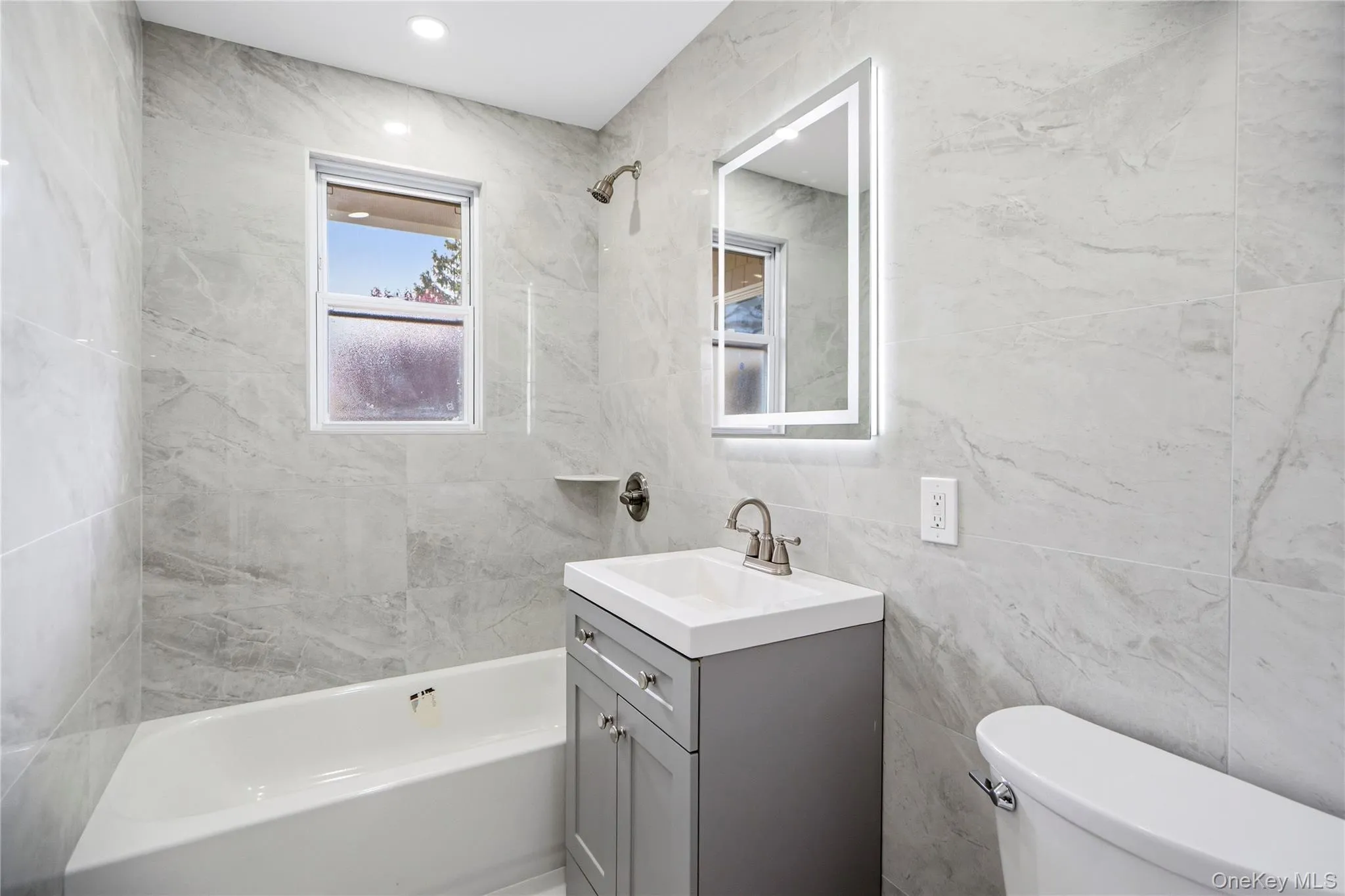Bathroom featuring a light gray vanity, integrated sink, and an illuminated mirrored medicine cabinet Bathroom featuring a light gray vanity, integrated sink, and an illuminated mirrored medicine cabinet