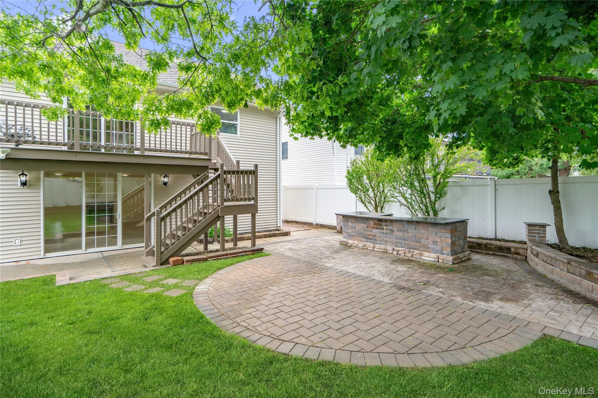 Expansive backyard featuring a circular paver patio, a built-in stone block counter, and a stone retaining wall Expansive backyard featuring a circular paver patio, a built-in stone block counter, and a stone retaining wall