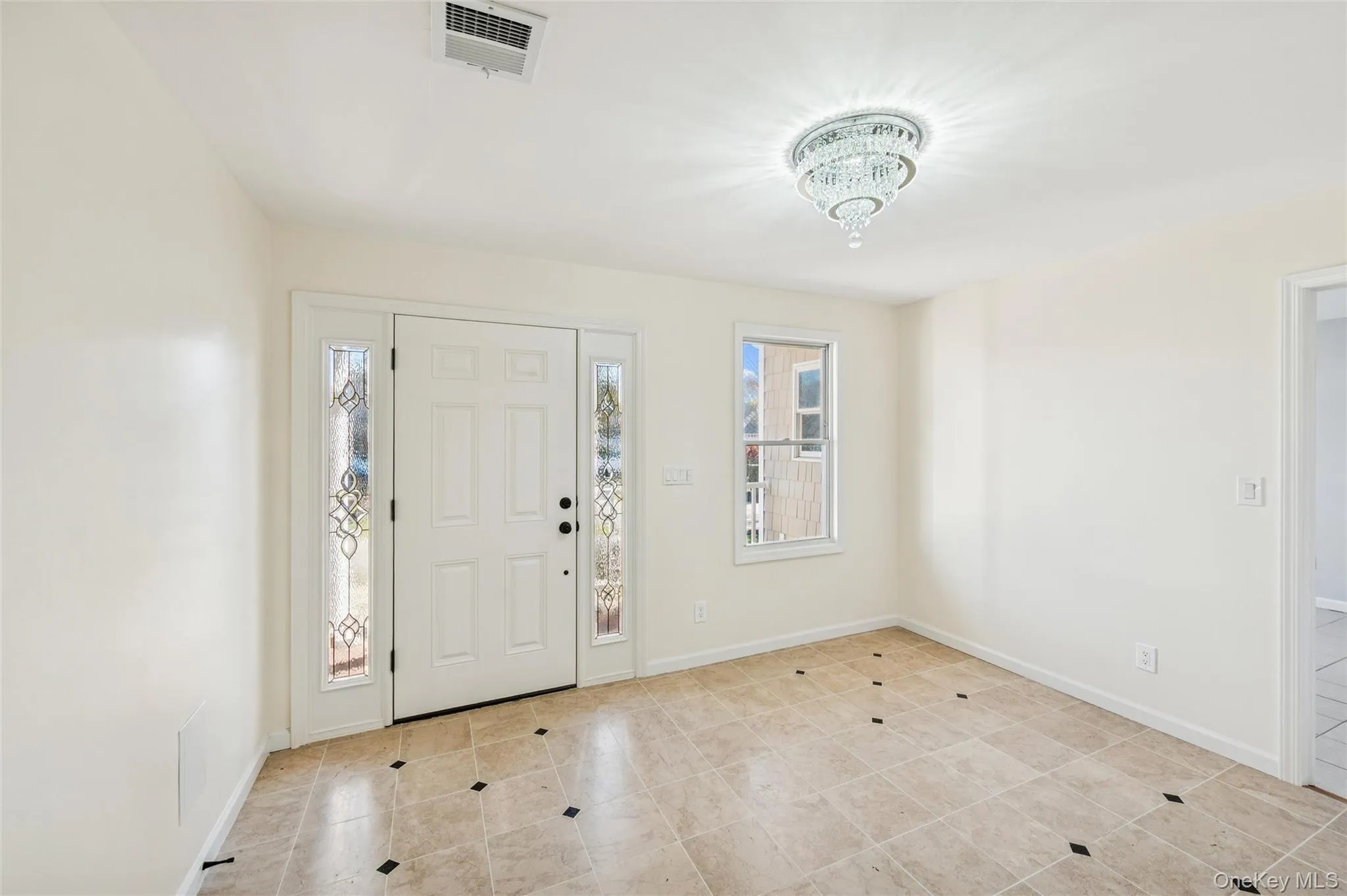 Entryway featuring a white paneled door with decorative sidelights, a tiered crystal chandelier, light-toned tiled flooring with dark accent tiles Entryway featuring a white paneled door with decorative sidelights, a tiered crystal chandelier, light-toned tiled flooring with dark accent tiles