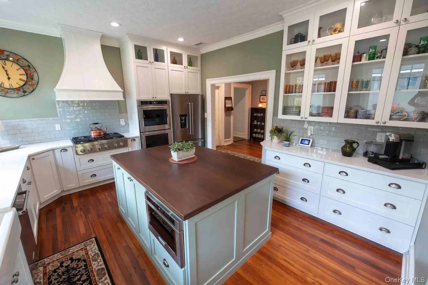 Hardwood flooring grounds this kitchen featuring a central island with a wood-finish countertop, white perimeter cabinetry, and an integrated stainless steel appliance suite Hardwood flooring grounds this kitchen featuring a central island with a wood-finish countertop, white perimeter cabinetry, and an integrated stainless steel appliance suite