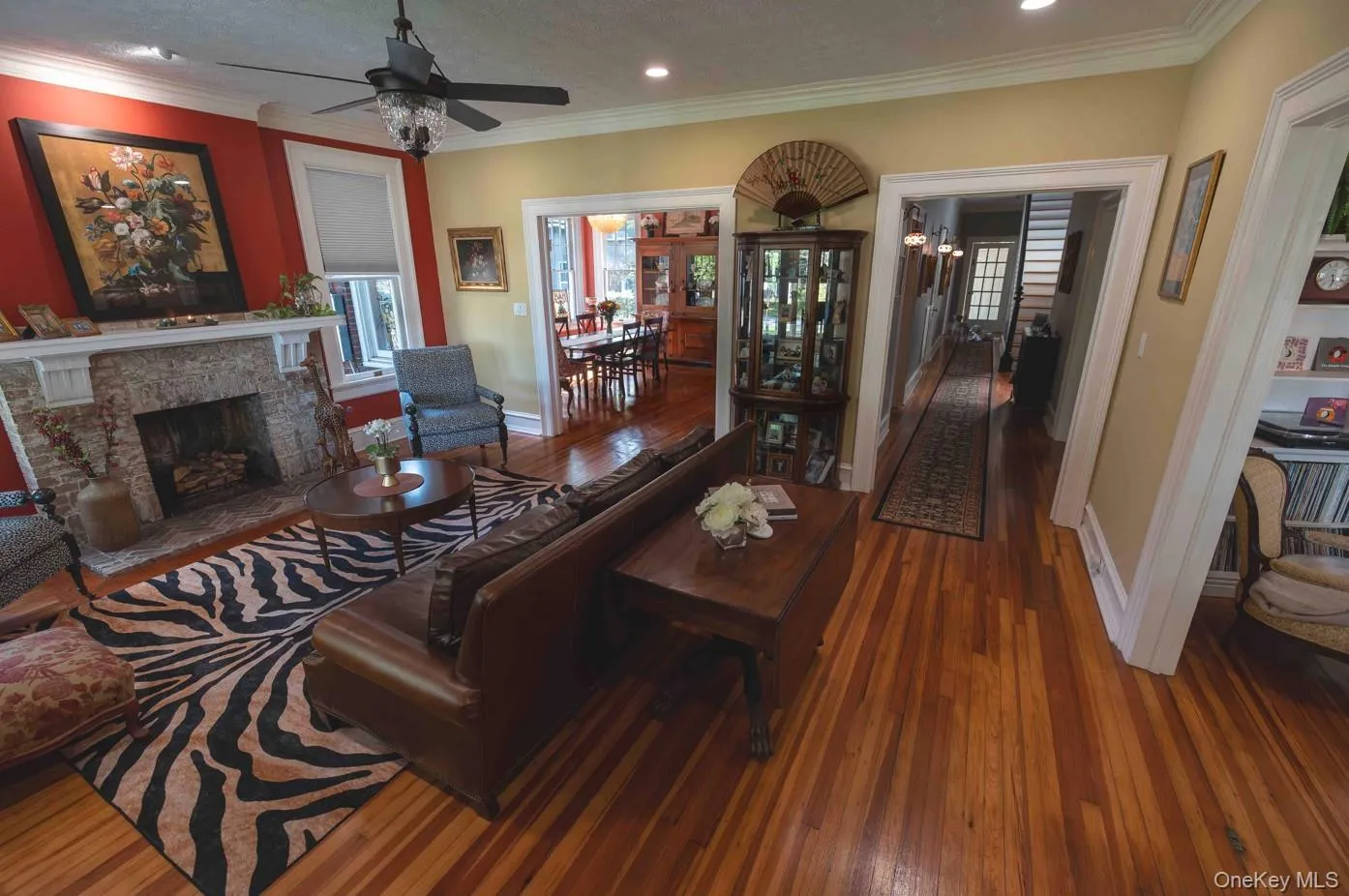 Hardwood flooring extends throughout this expansive living area, featuring a stone fireplace with a decorative mantel and a ceiling fan with integrated lighting and stunning fireplace Hardwood flooring extends throughout this expansive living area, featuring a stone fireplace with a decorative mantel and a ceiling fan with integrated lighting and stunning fireplace