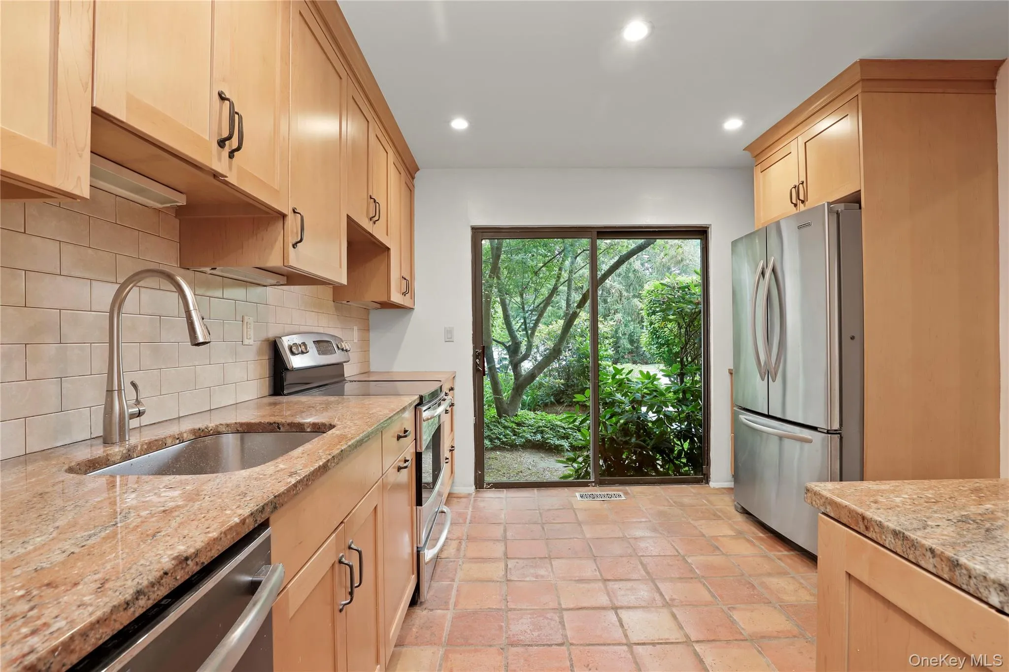 Kitchen with appliances with stainless steel finishes, a sink, decorative backsplash, light brown cabinetry, and light stone countertops Kitchen with appliances with stainless steel finishes, a sink, decorative backsplash, light brown cabinetry, and light stone countertops
