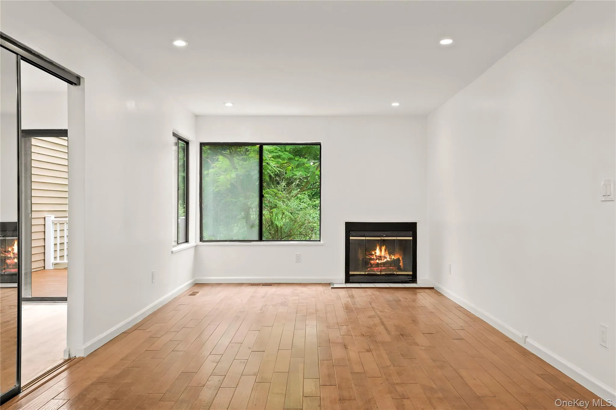 Unfurnished living room featuring light wood-type flooring, a glass covered fireplace, recessed lighting, and baseboards Unfurnished living room featuring light wood-type flooring, a glass covered fireplace, recessed lighting, and baseboards