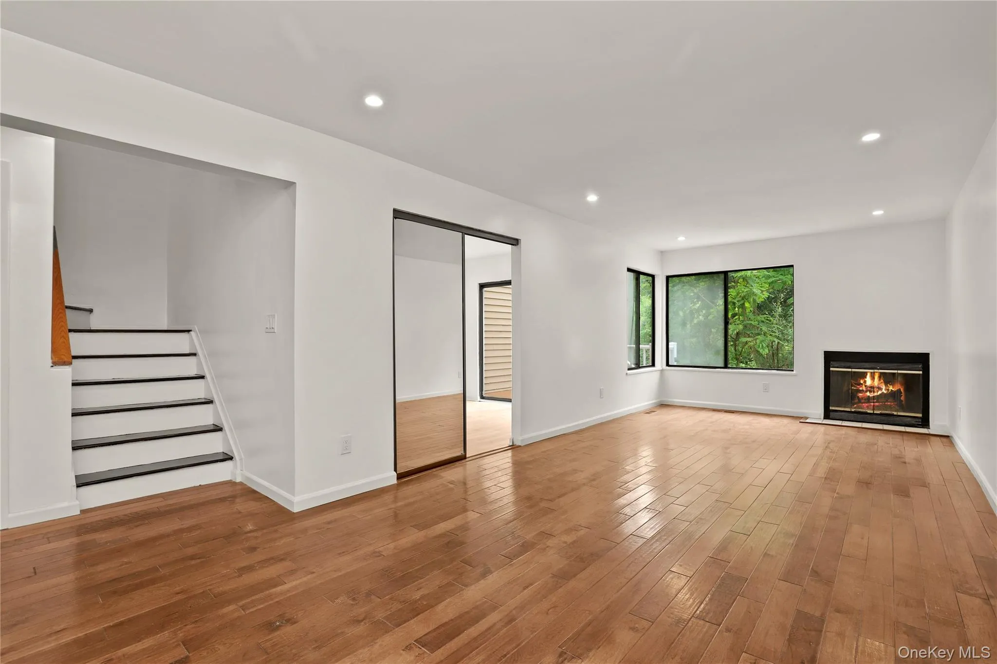 Unfurnished living room with light wood-style floors, a glass covered fireplace, stairs, recessed lighting, and baseboards Unfurnished living room with light wood-style floors, a glass covered fireplace, stairs, recessed lighting, and baseboards