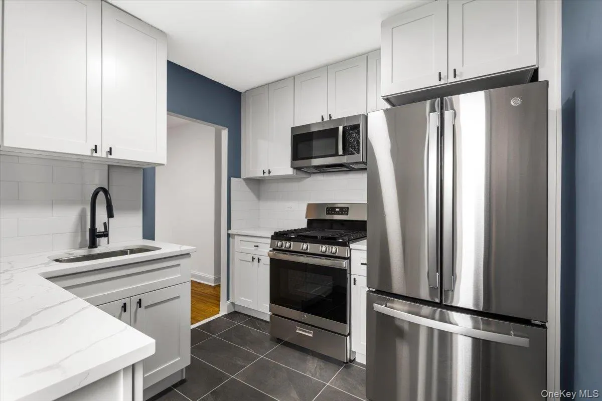 Kitchen featuring white shaker cabinetry, stainless steel appliances, white subway tile backsplash, white countertops, and dark tile flooring Kitchen featuring white shaker cabinetry, stainless steel appliances, white subway tile backsplash, white countertops, and dark tile flooring