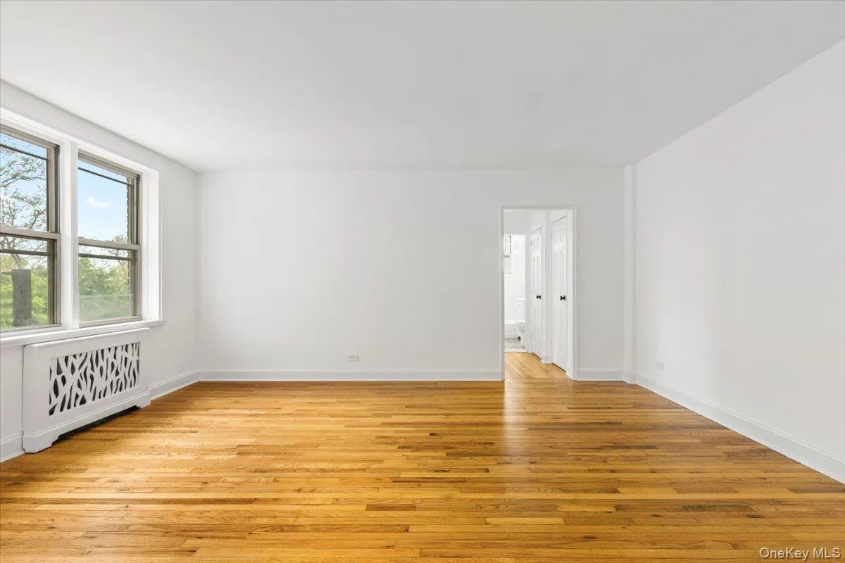 Hardwood flooring throughout this spacious living room, featuring white walls, a large window, and a decorative radiator cover Hardwood flooring throughout this spacious living room, featuring white walls, a large window, and a decorative radiator cover